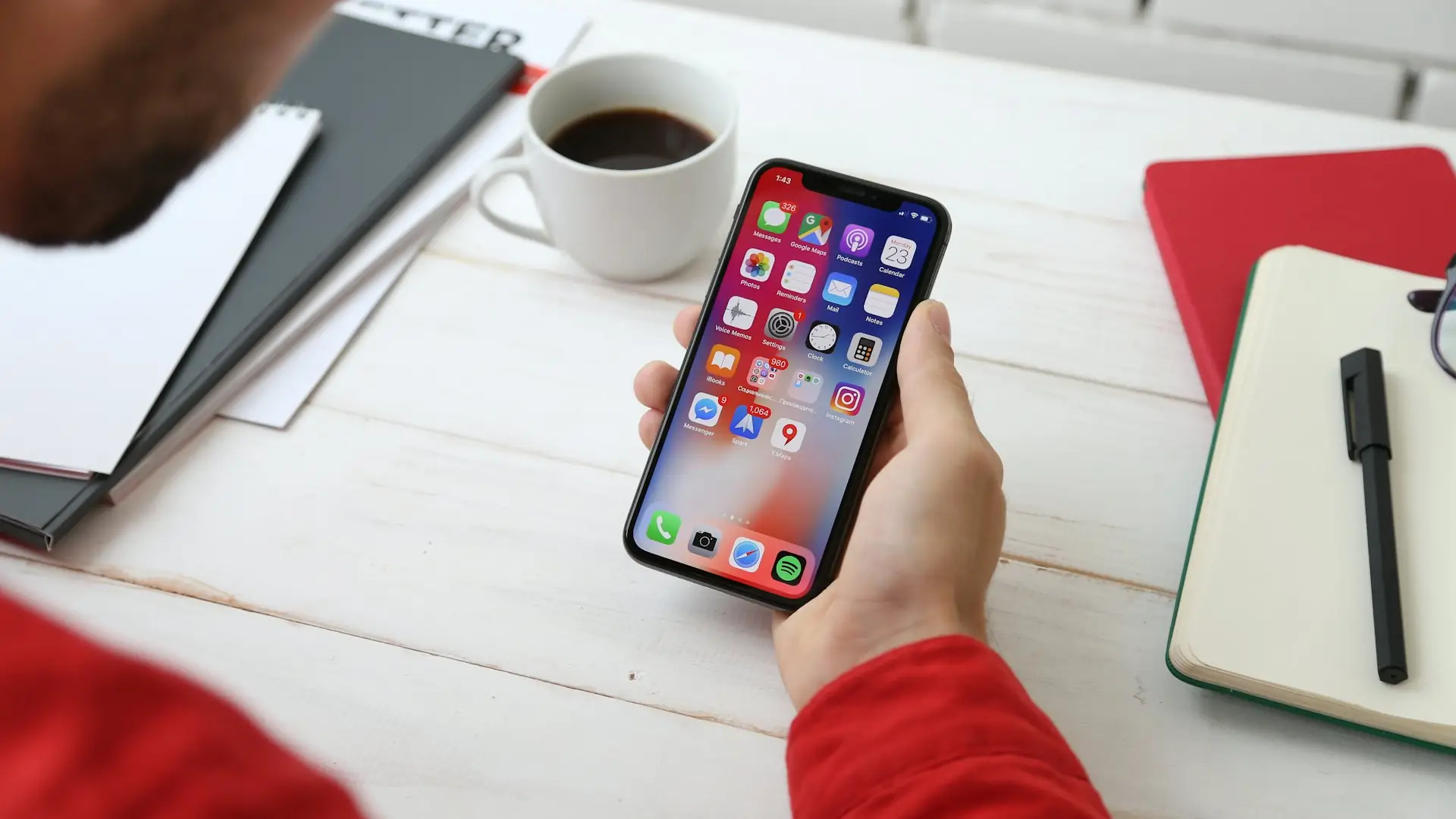 Person holding a smartphone at a desk with coffee and a notebook