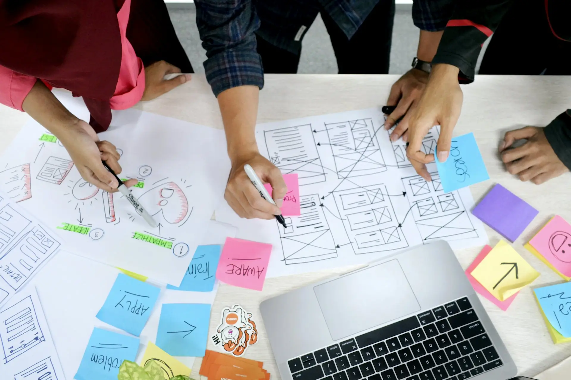 Designers sketching wireframes with sticky notes beside a laptop