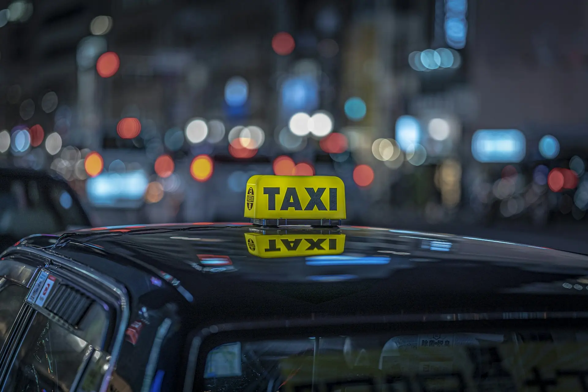 Illuminated taxi sign on a car roof at night with city lights behind